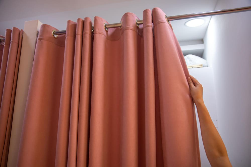 En person håller en rosa gardin i ett badrum.